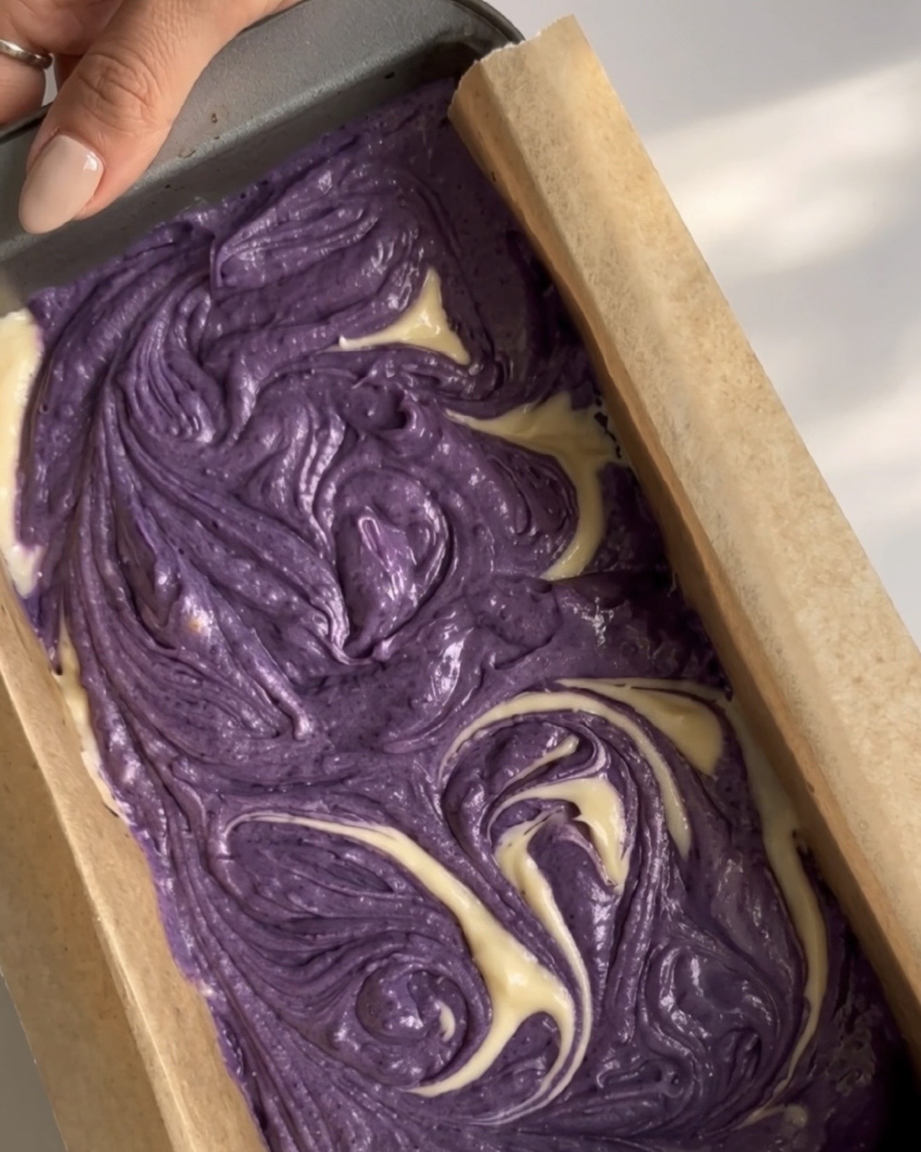 Impasti viola e vaniglia vorticati insieme a formare un motivo marmorizzato nello stampo da plumcake per il plumcake ube marmorizzato Ube Nolia