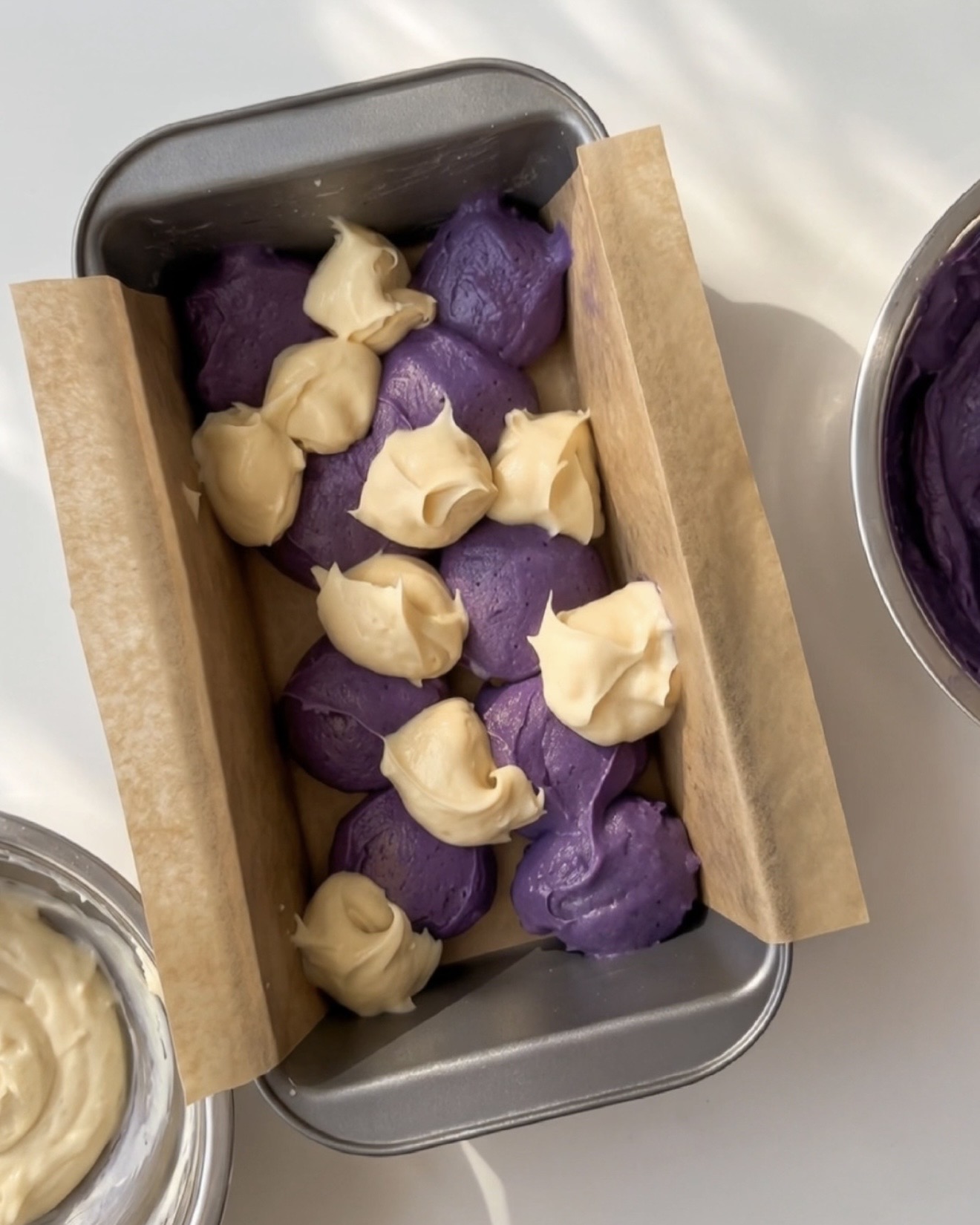 Cucchiaiate di impasto ube viola e impasto alla vaniglia alternati in uno stampo da plumcake foderato per il plumcake ube marmorizzato Ube Nolia