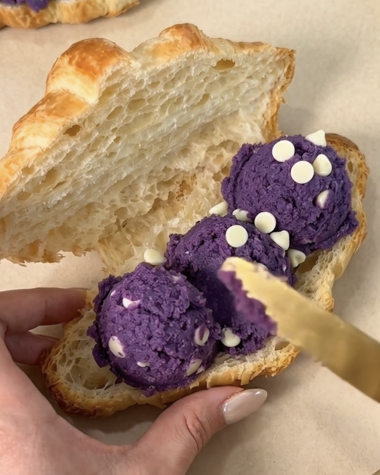 Spalmare l'impasto per biscotti ube (purple yam) e cioccolato bianco di Ube Nolia all'interno di un croissant da forno al burro tagliato per fare un ube crookie
