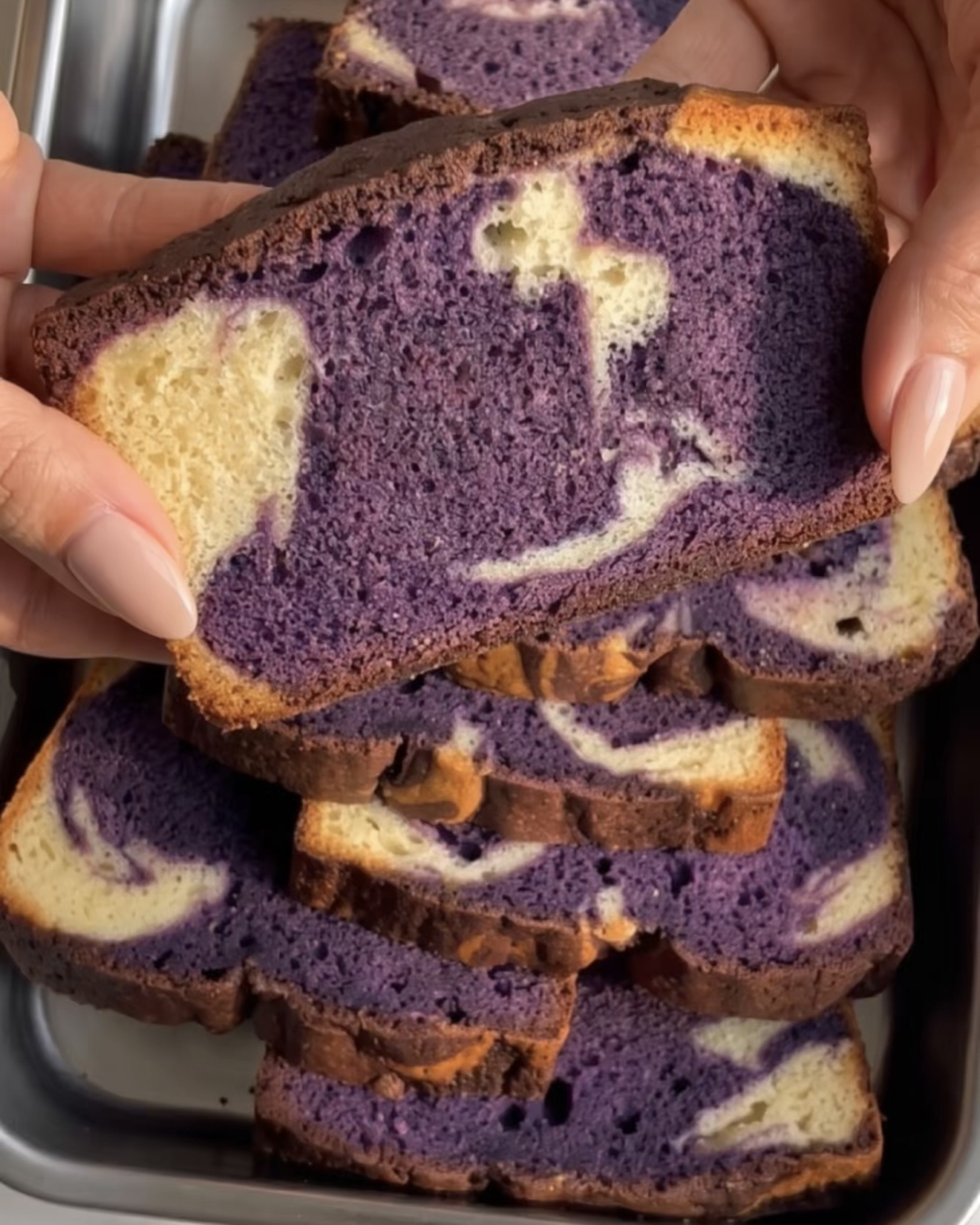 Mano che tiene una fetta di plumcake marmorizzato ube con una spirale viola e vaniglia, cotto con la polvere di ube UBE NOLIA®
