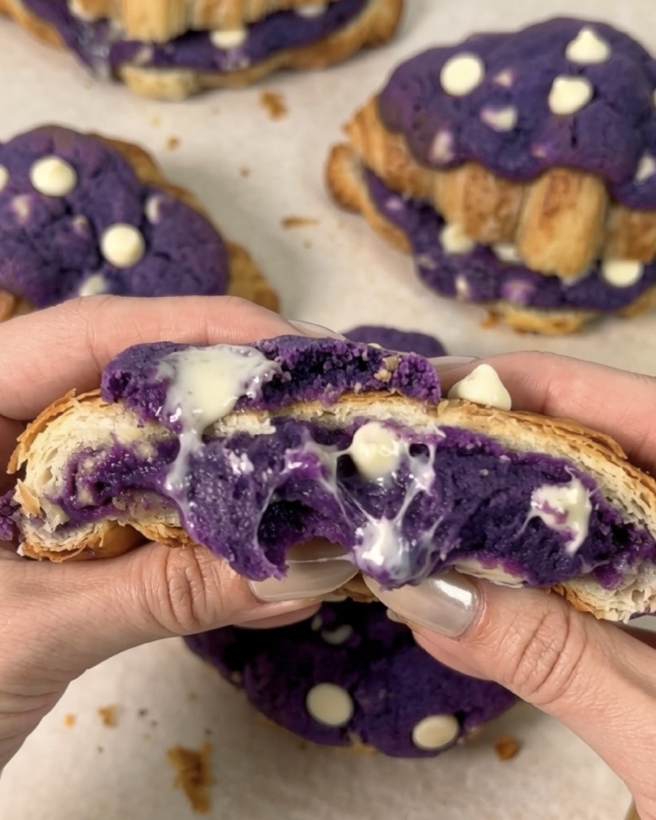 Ube crookies Ube Nolia appena sfornati aperti per rivelare un centro di biscotto ube (purple yam) e cioccolato bianco viola fuso che cola tra strati di croissant dorati