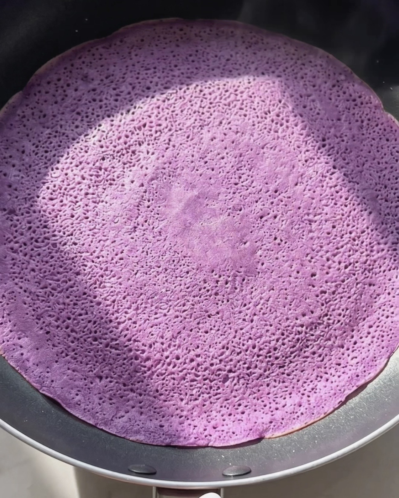 Cottura di una sottile crepe ube dadar gulung viola in una padella antiaderente
