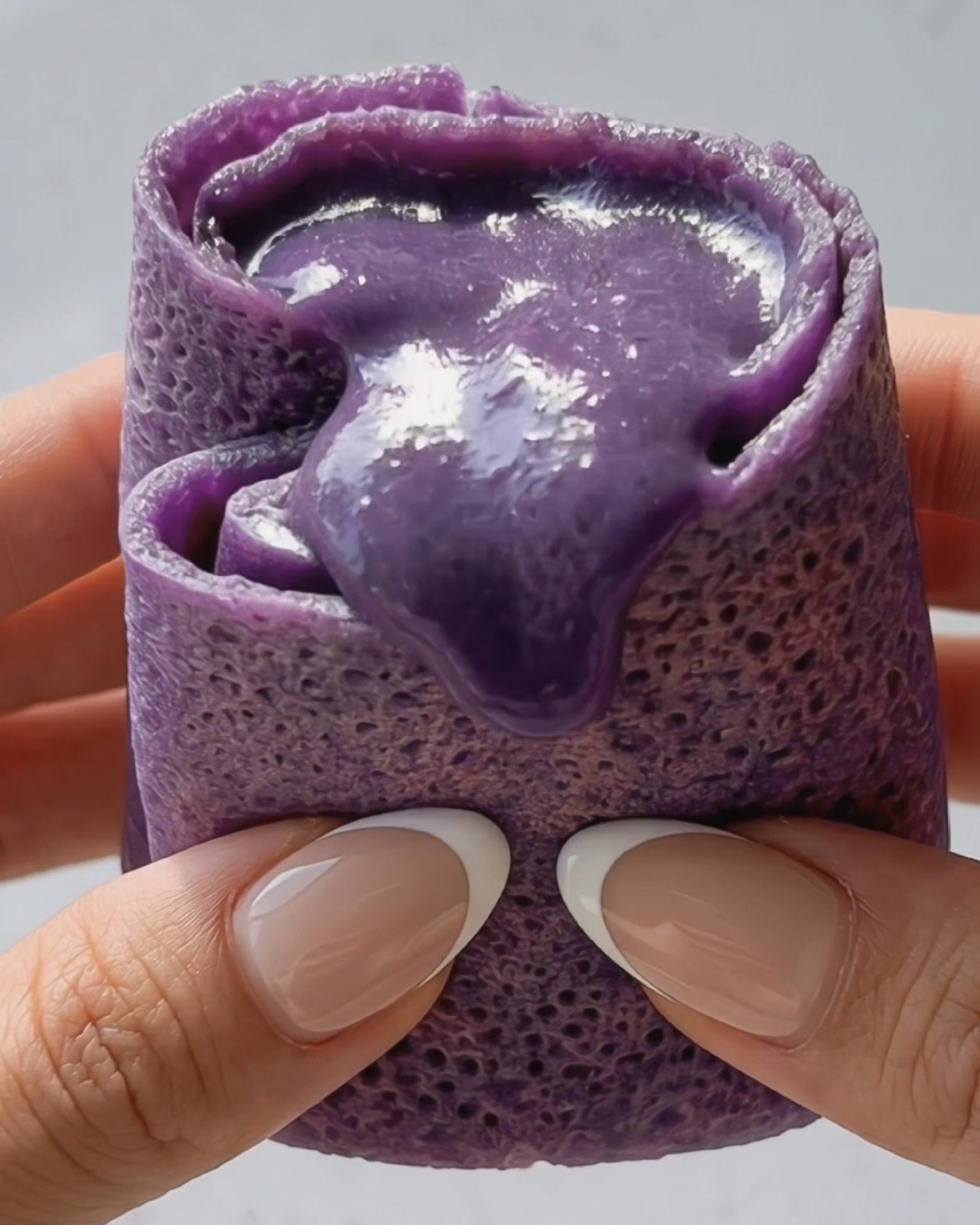 Crepe ube dadar gulung tagliata che mostra il ripieno di ube halaya viola setoso e cremoso all'interno