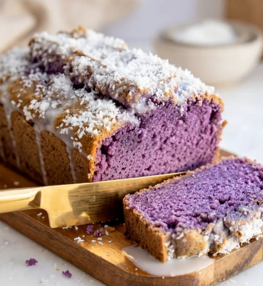 Fetta di plumcake viola ube cocco su un tagliere di legno con topping di cocco bianco e un coltello dorato, ricetta UBE NOLIA