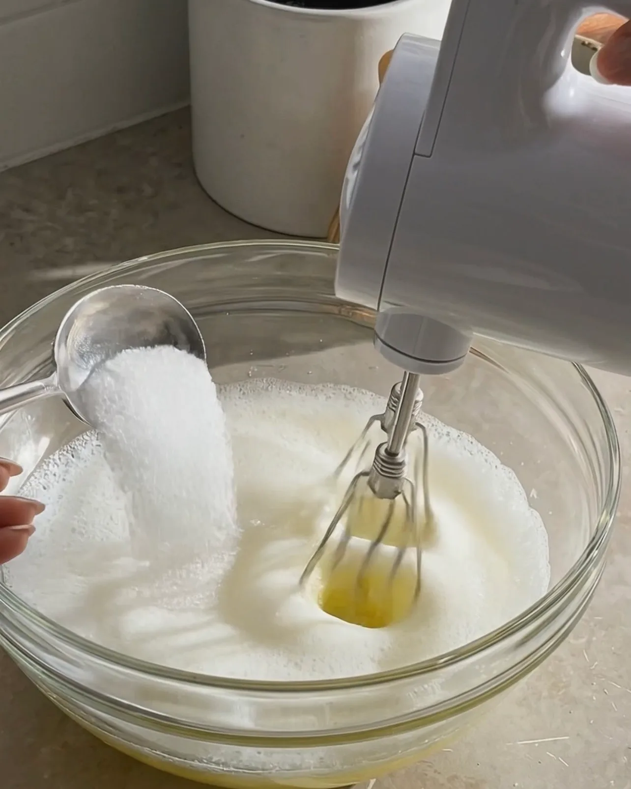 Aggiungere zucchero agli albumi spumosi mentre si montano con un mixer elettrico per la ube roll cake di Ube Nolia