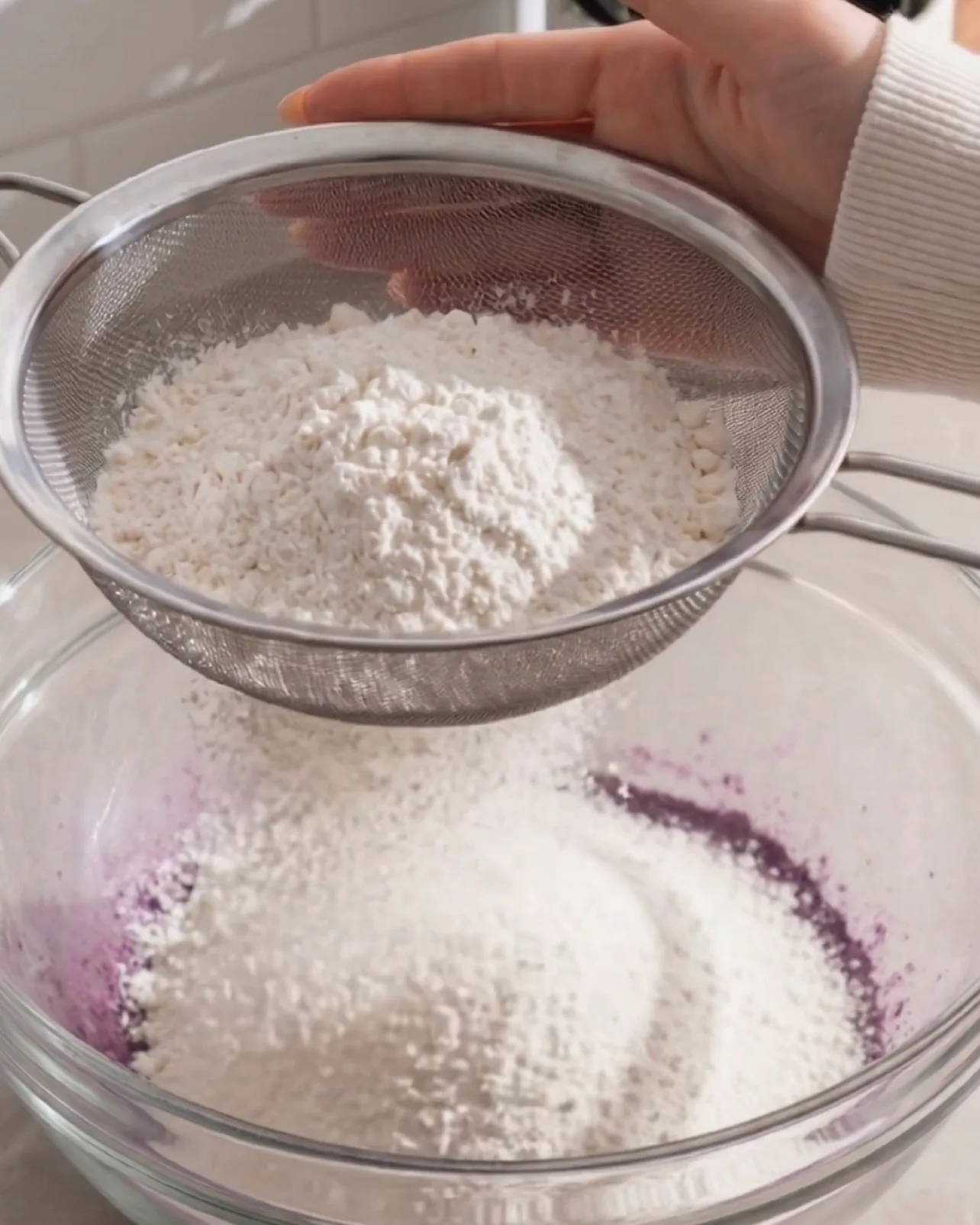 Setacciare farina per torte nell'impasto viola all'ube attraverso un setaccio a maglie fini di Ube Nolia
