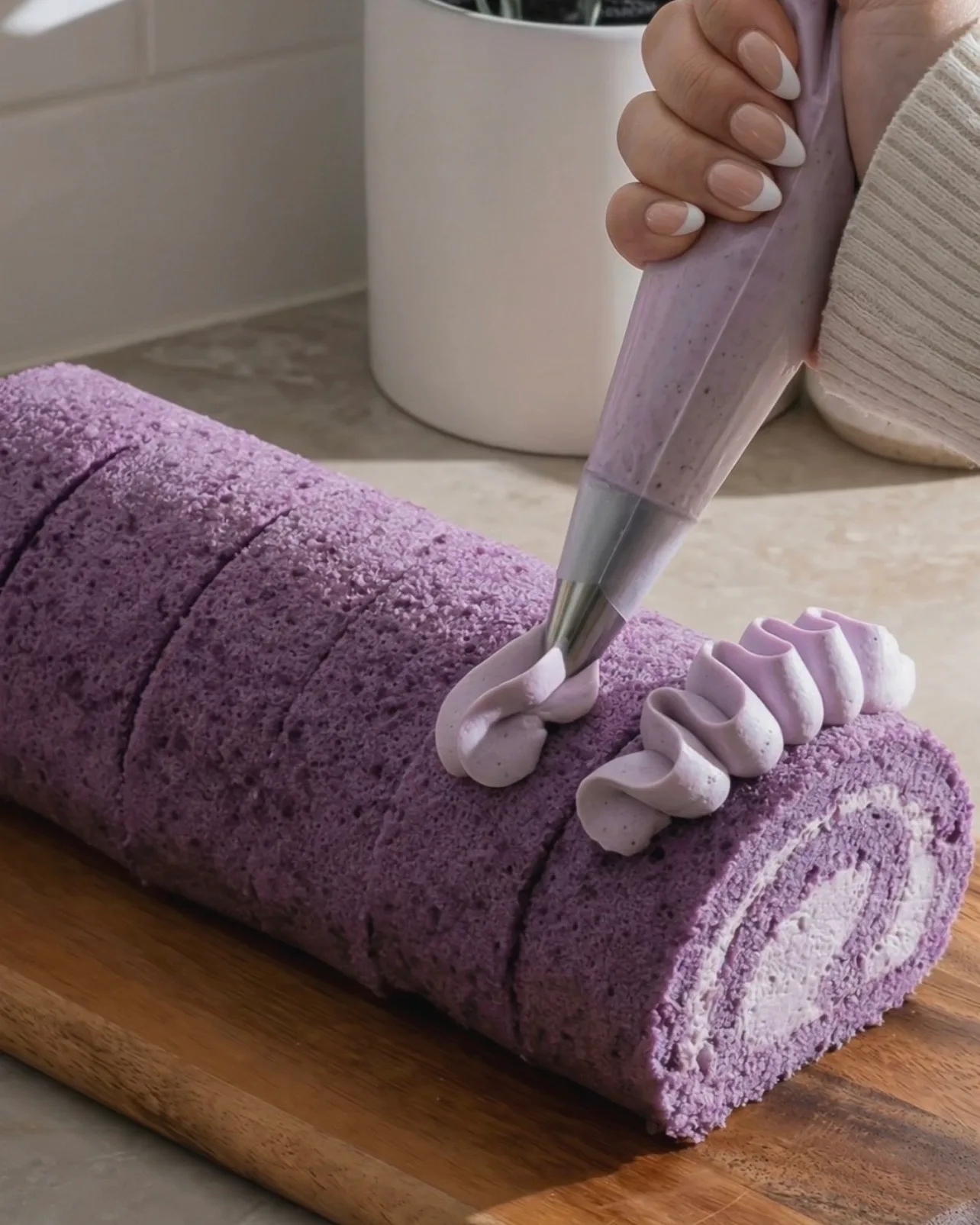 Decorare con rosette di panna montata all'ube sulla parte superiore del rotolo di ube cake viola finito di Ube Nolia