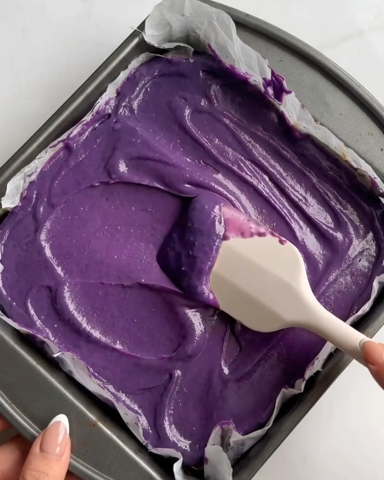 La vivida ganache ube al cioccolato bianco viola viene spalmata sullo strato di kataifi al pistacchio per le barrette brownie al cioccolato Ube Dubai di Ube Nolia